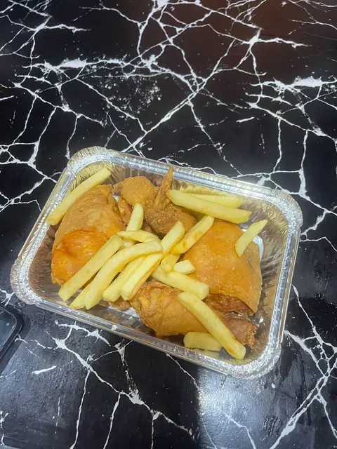 A foil tray of broast and fries on a dark table.