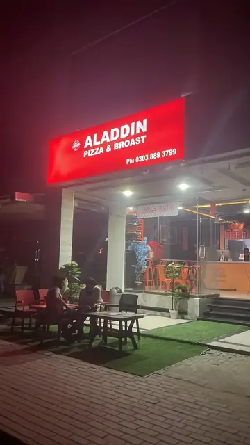 Aladdin Pizza & Broast at night, with the red sign lit and outdoor seating.